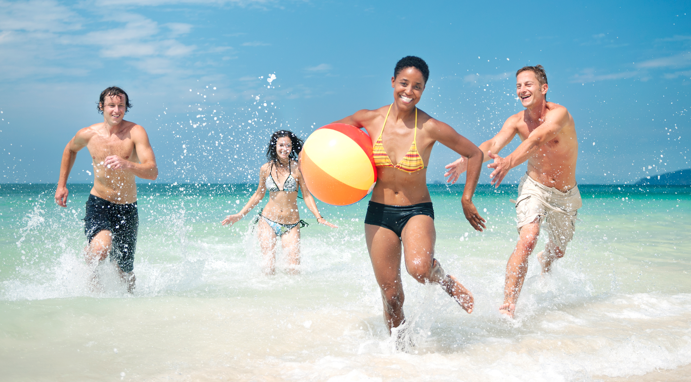 A group of friends plays with a beach ball on the beach in shallow ocean water.