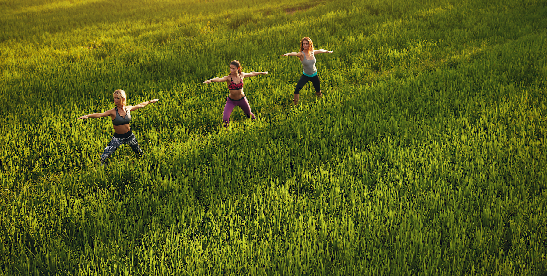 Three women doing yoga in a field during the summer.