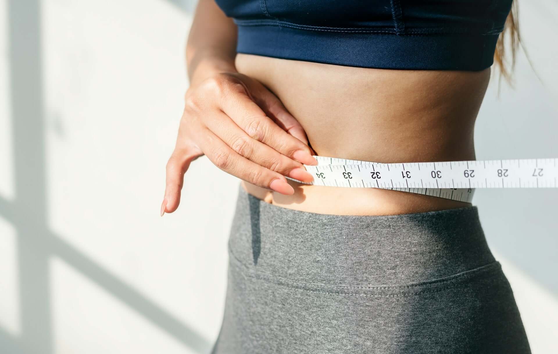 A woman measuring her stomach to indicate weight loss and waistline measurement.