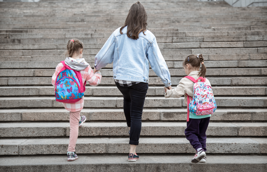 A mother takes two of her children to school, walking up a large staircase.