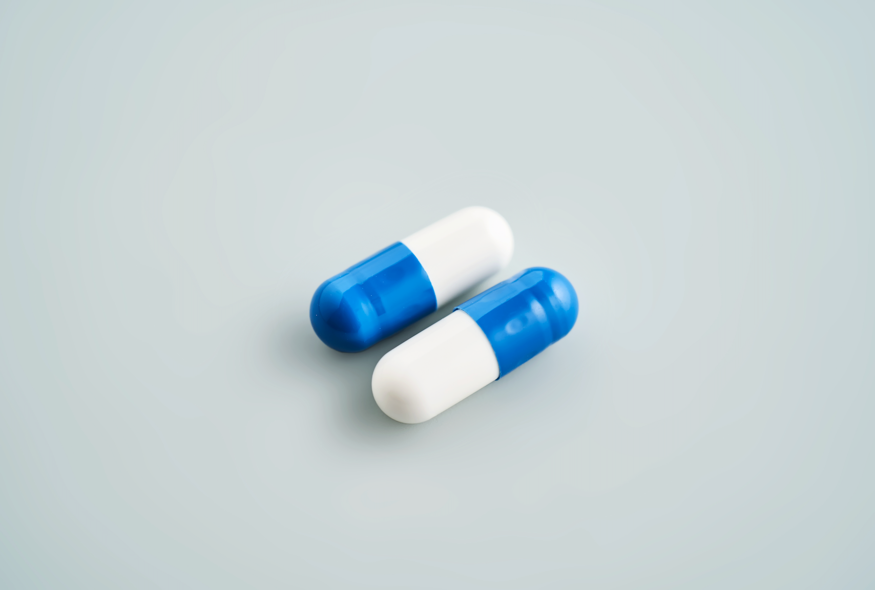 Blue and white pill capsules on plain grey background.
