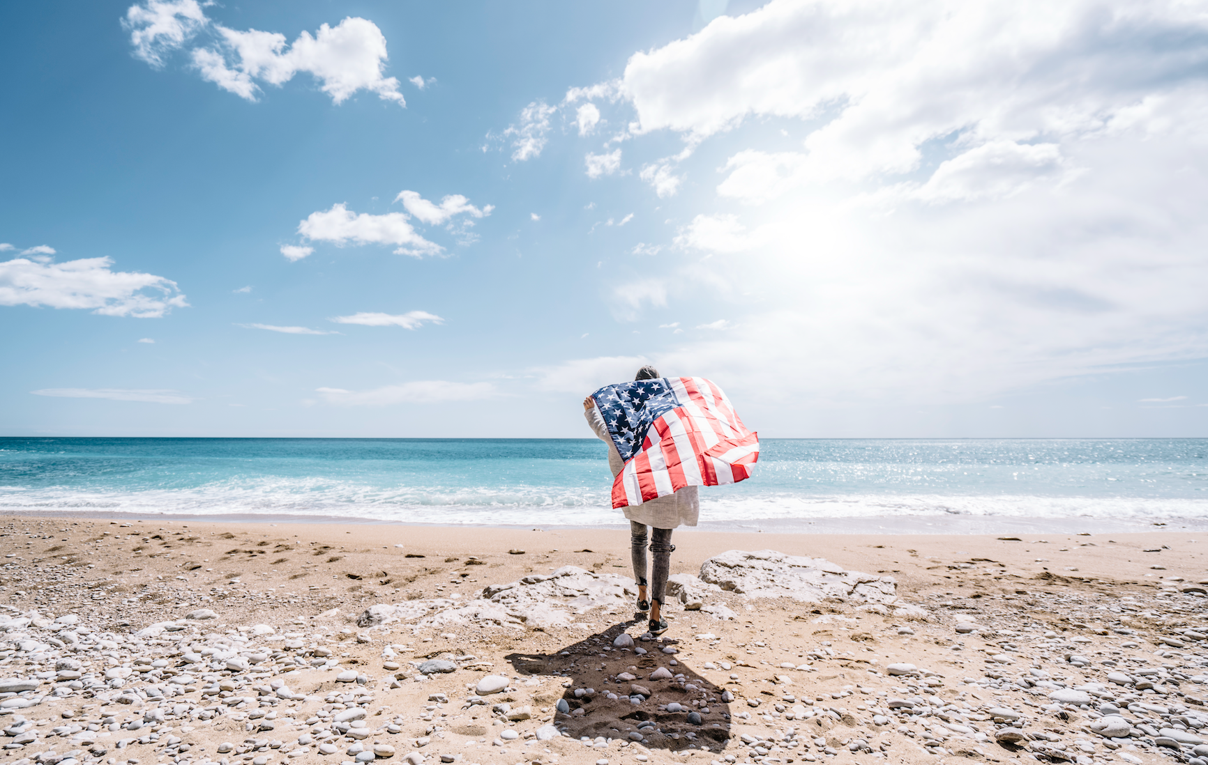 July 2026 monthly specials hero image with a woman carrying an American flag on a beach.