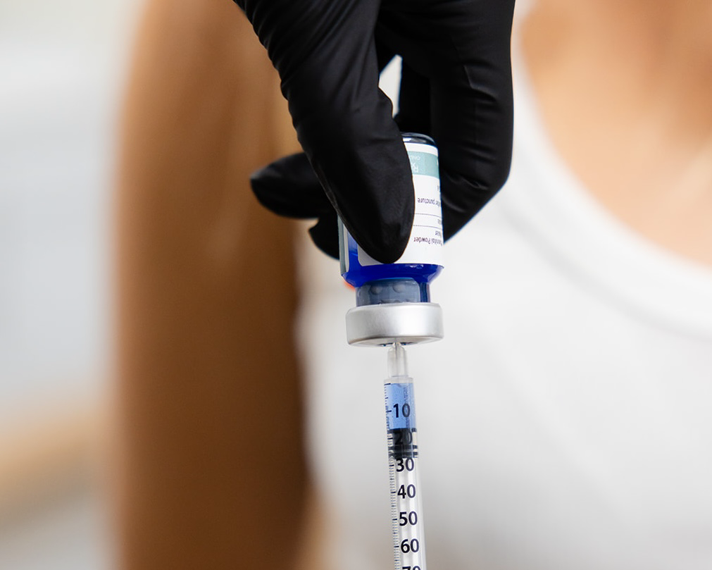 A syringe pulling a dose of a blue peptide from an upside-down vial.