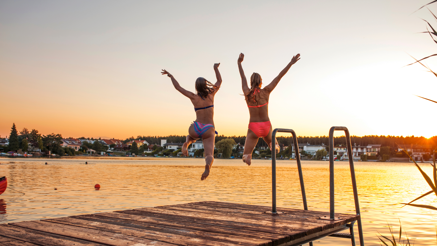 Two women jumping off a lake dock at sunset in June