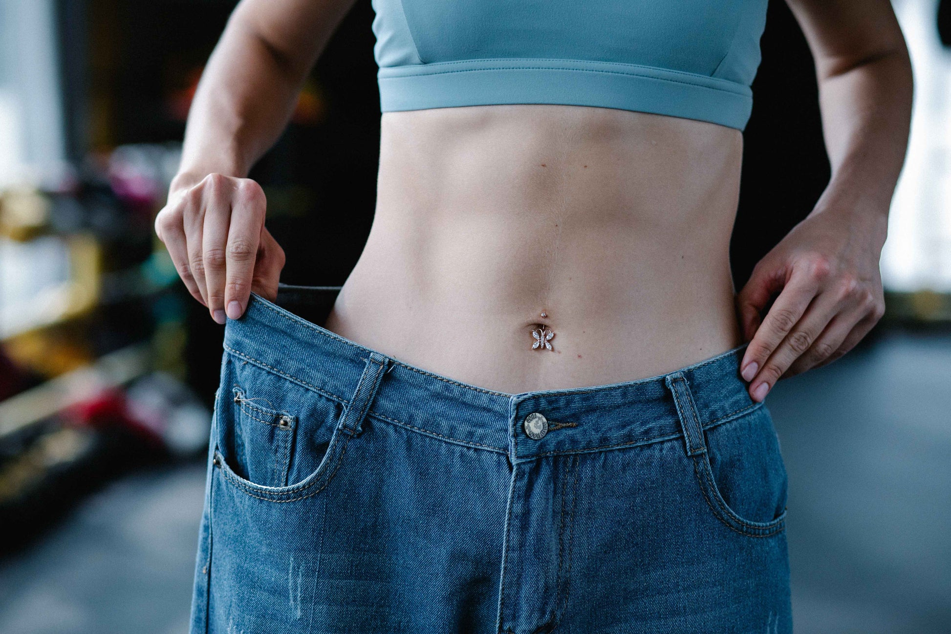 A woman holds out oversized jeans to indicate significant weight loss and fat burning.